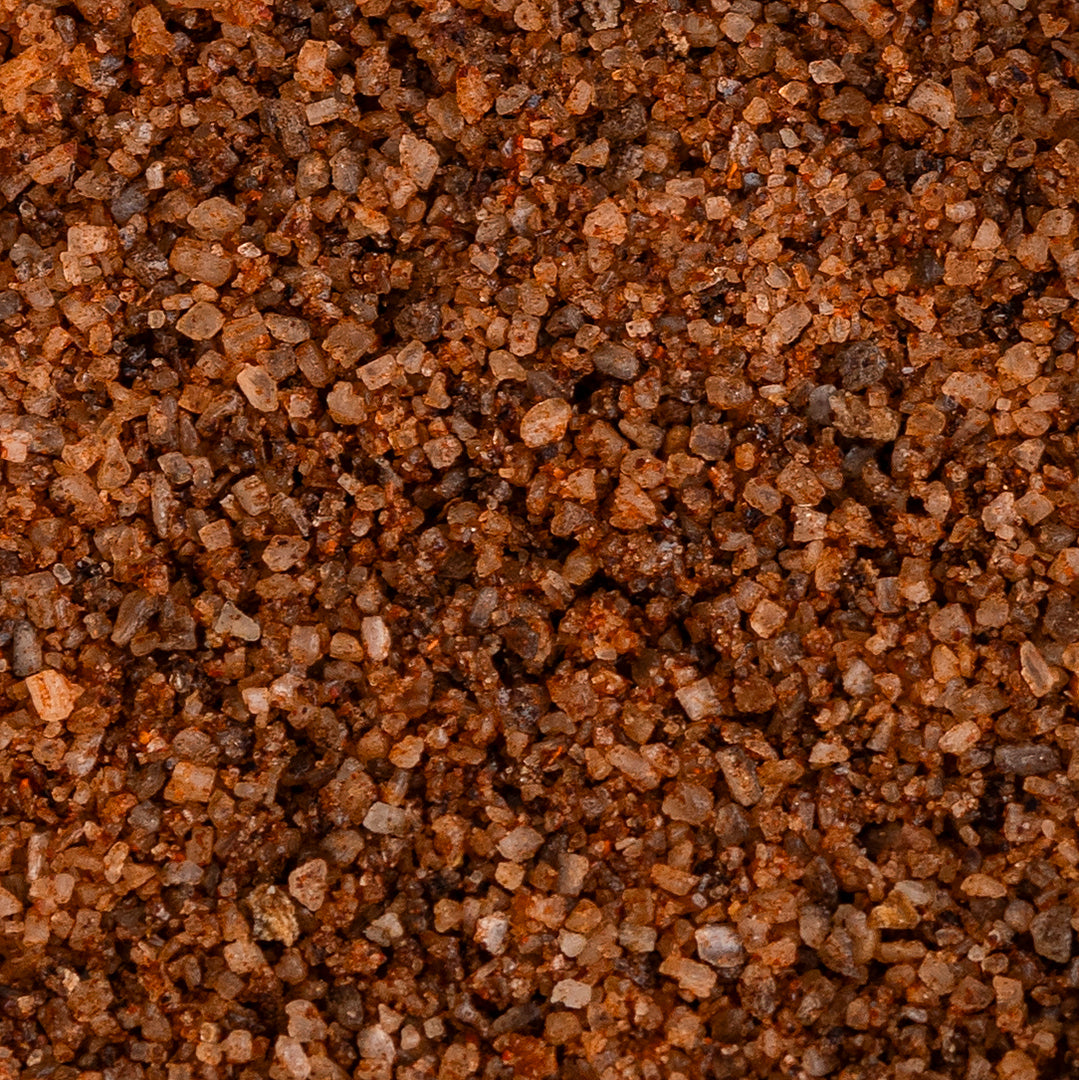 Macro close-up of Texas Salt Co. Chile Lime Smoked Salt showing coarse reddish-brown crystals infused with chili and lime.