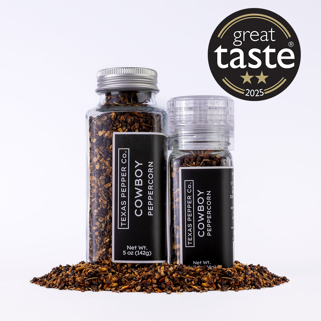 Two glass jars of Texas Pepper Co. Cowboy Peppercorn (2.25 oz grinder and 5 oz jar) with spilled smoked peppercorn blend in front.