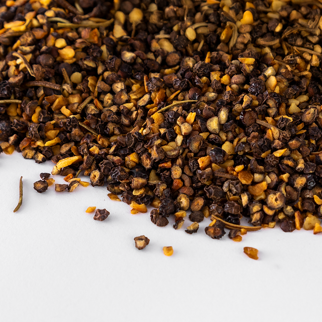Close-up of Cowboy Peppercorn blend showing smoked cracked black pepper, dried garlic, and dried rosemary on white background.