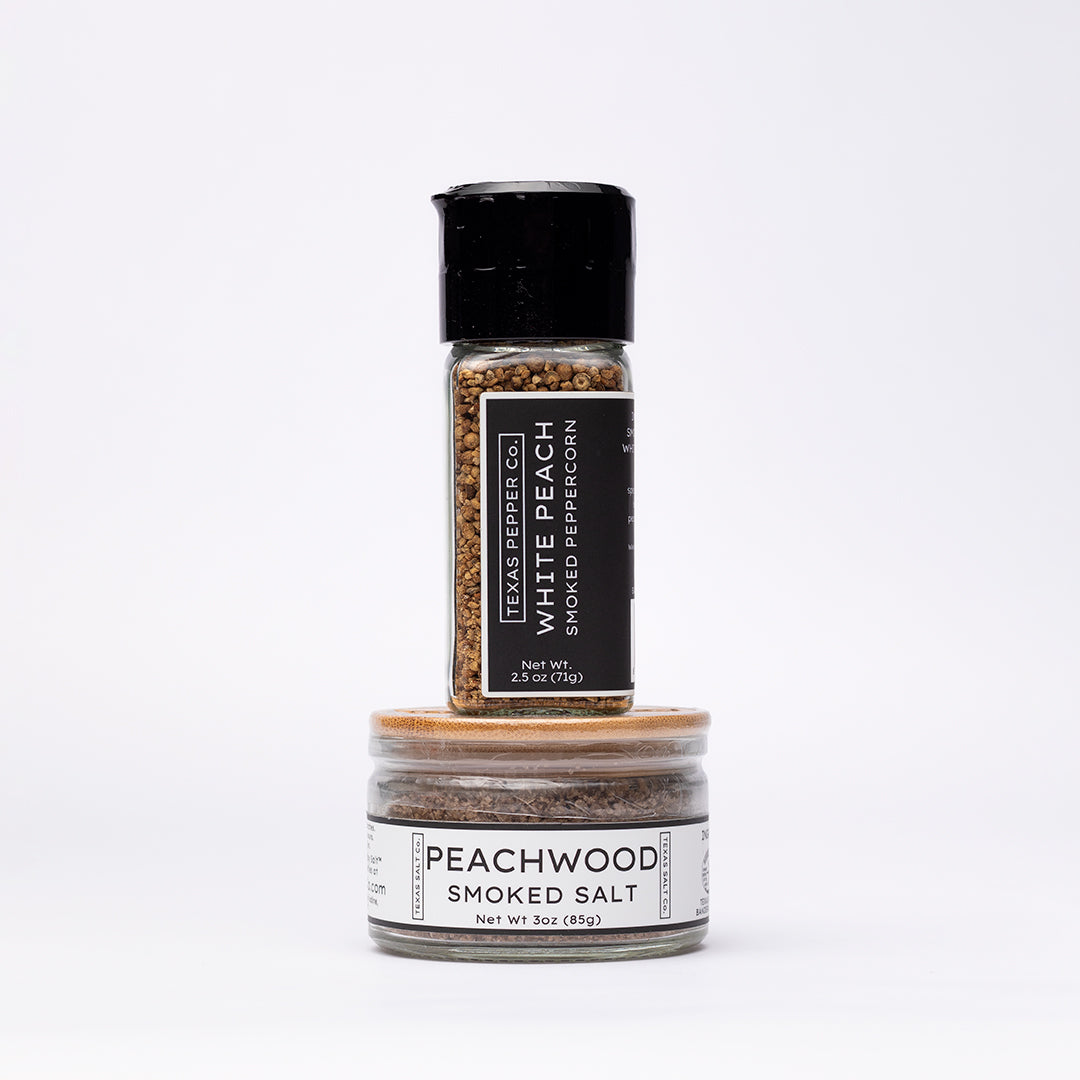 White Peach Smoked Peppercorn with grinder top stacked over Peachwood Smoked Salt jar with flat bamboo lid and clean white labels