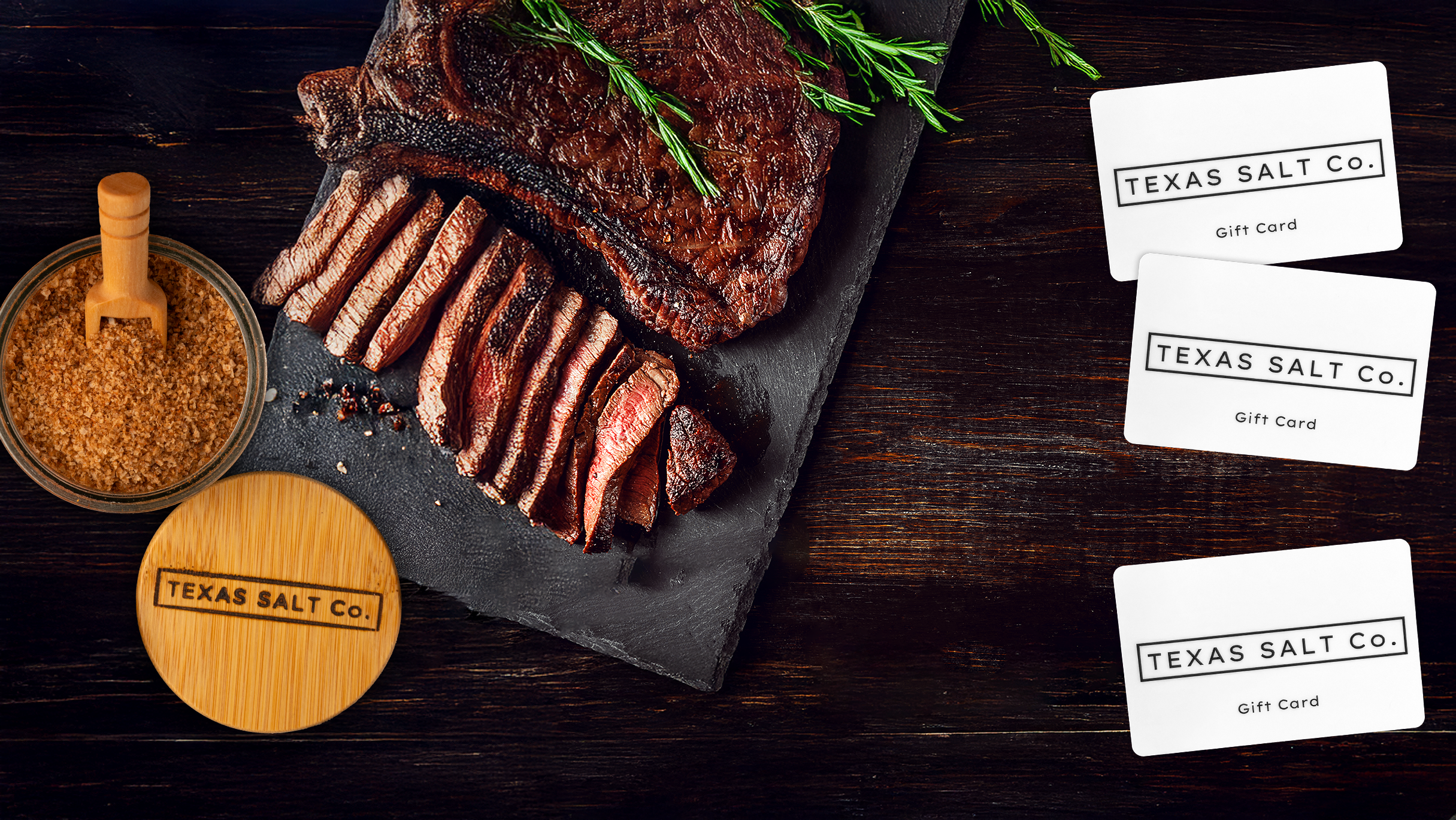 Sliced steak on a slate board with a Texas Salt Co. Smoked Cayenne Salt jar and Texas Salt Co. gift cards.