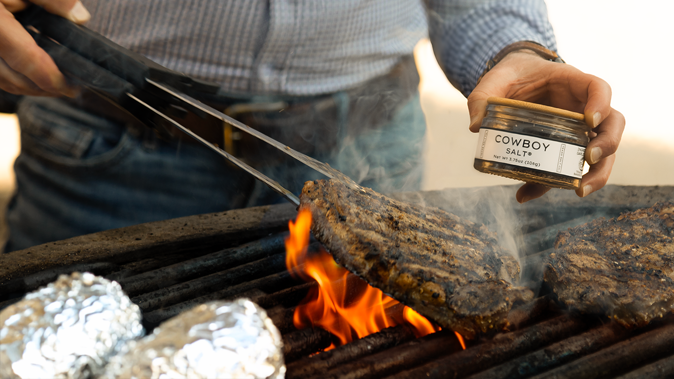 Person grilling food with a jar labeled 'Cowboy Grits' in the background