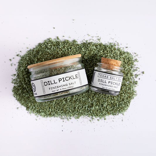 Dill Pickle Finishing Salt set by Texas Salt Co. – includes 1oz cork top and 3.75oz pinch jar on a bed of green salt.