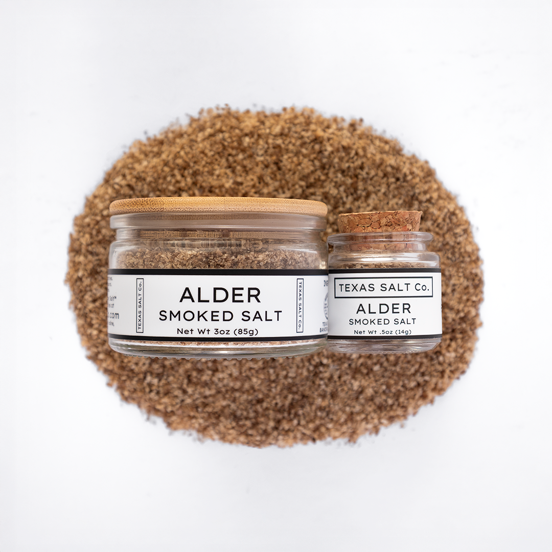 Texas Salt Co. Alder Smoked Salt 3oz and .5oz jars displayed on top of a circular pile of alder-smoked salt in a top-down composition.