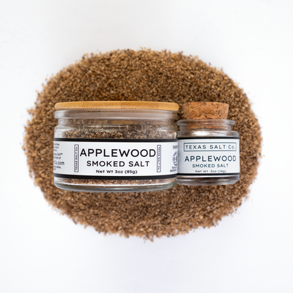 Texas Salt Co. Applewood Smoked Salt 3oz and .5oz jars displayed on top of a circular pile of applewood-smoked salt in a top-down composition.