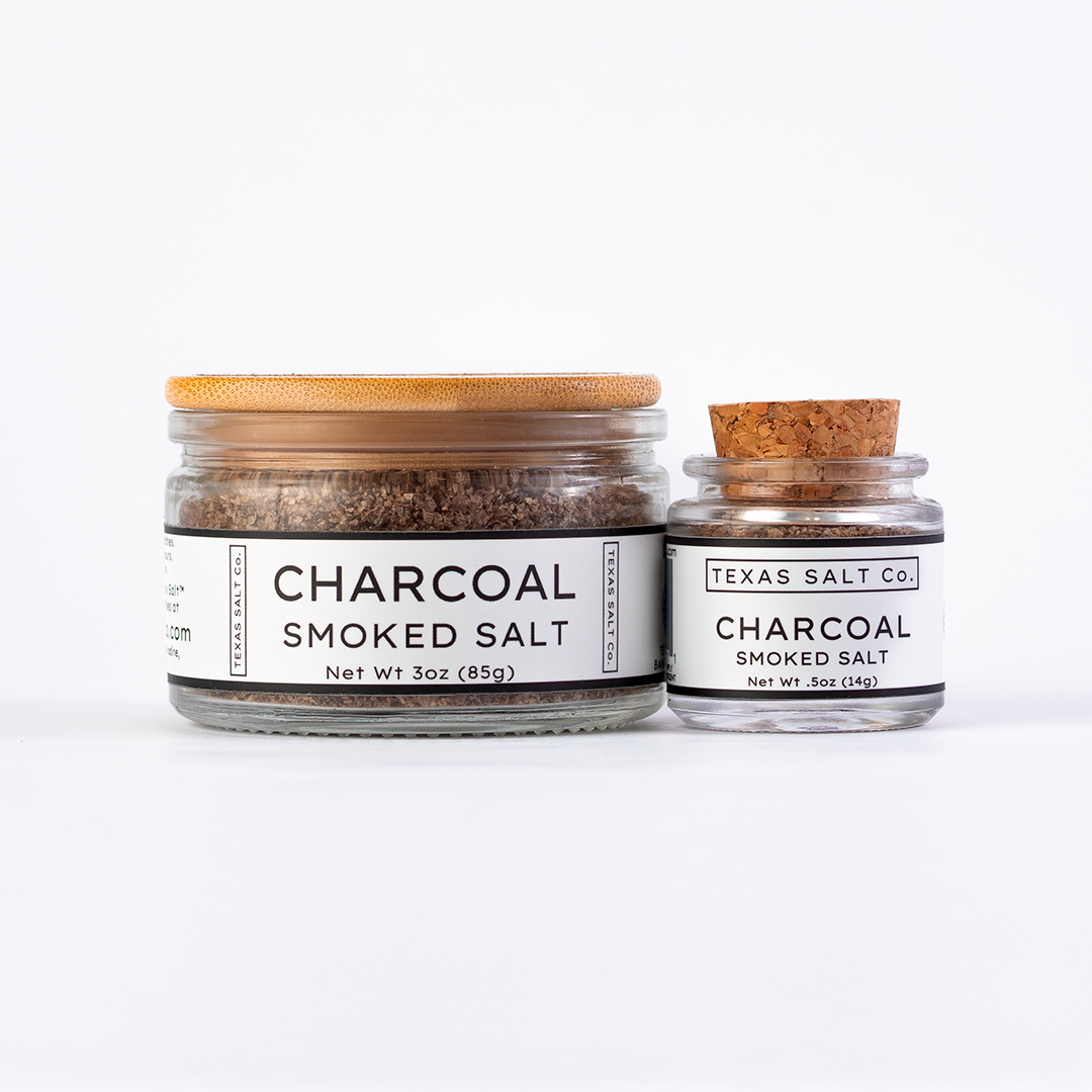 Texas Salt Co. Charcoal Smoked Salt in 3oz bamboo-lid jar and .5oz cork-top jar displayed side by side on a white background.