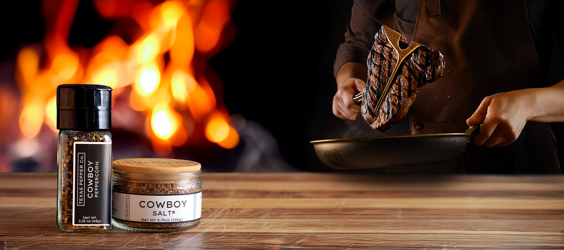 Cowboy Salt and Cowboy Peppercorn bundle in front of a wood table and open flame, with a T-bone steak being flipped in a skillet by hand—Father’s Day gift set from Texas Salt Co.
