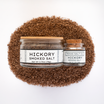 Texas Salt Co. Hickory Smoked Salt 2.75oz and .5oz jars displayed on top of a circular pile of hickory-smoked salt in a top-down composition.