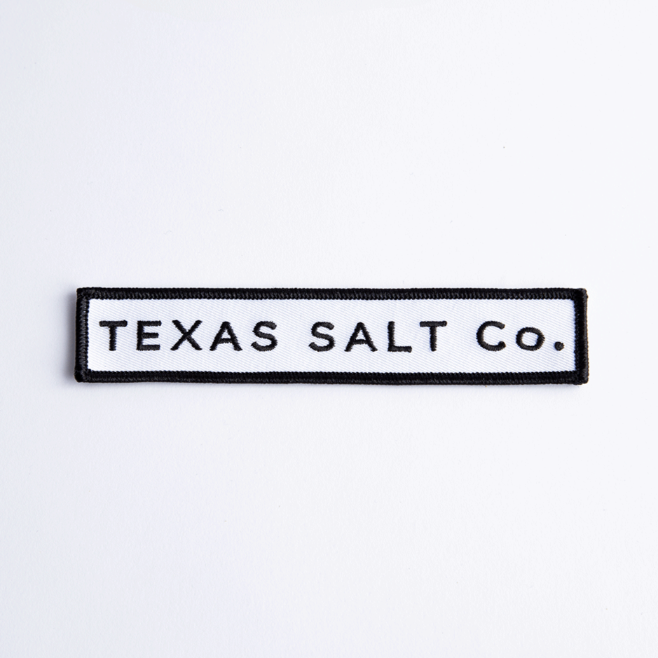 Close-up of rectangular black and white iron-on patch with text "TEXAS SALT CO." on white background