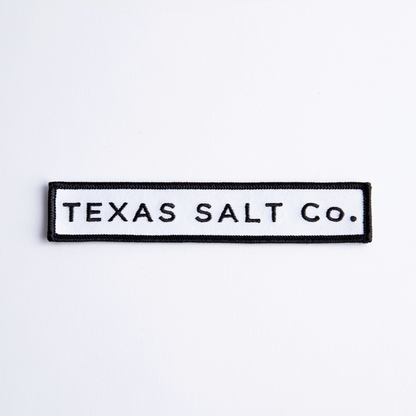 Close-up of rectangular black and white iron-on patch with text "TEXAS SALT CO." on white background
