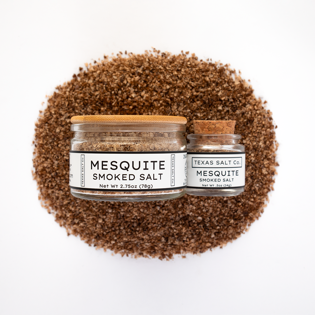 Texas Salt Co. Mesquite Smoked Salt 2.75oz and .5oz jars displayed on top of a circular pile of mesquite-smoked salt in a top-down composition.