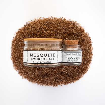 Texas Salt Co. Mesquite Smoked Salt 2.75oz and .5oz jars displayed on top of a circular pile of mesquite-smoked salt in a top-down composition.