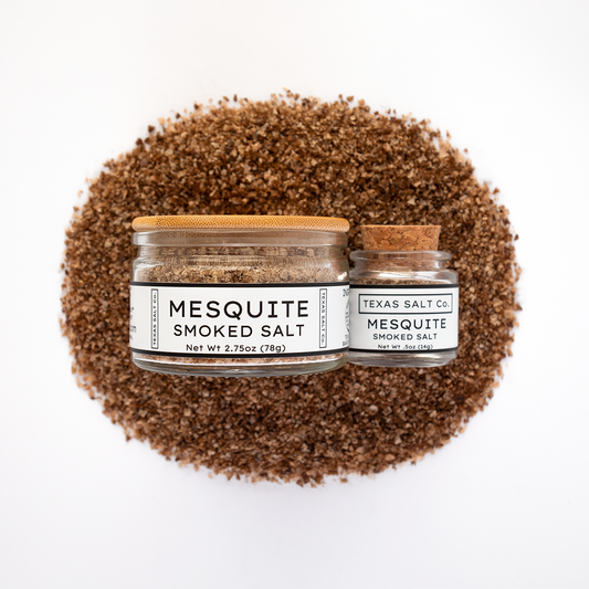 Texas Salt Co. Mesquite Smoked Salt 2.75oz and .5oz jars displayed on top of a circular pile of mesquite-smoked salt in a top-down composition.