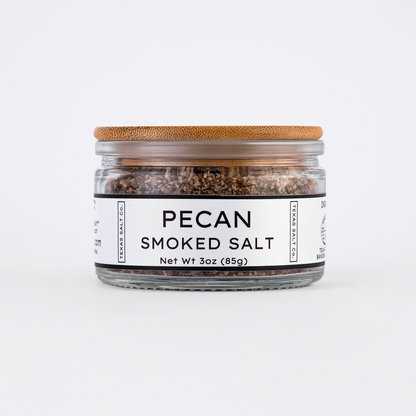 Glass jar of Texas Salt Co. Pecan Smoked Salt, 3 oz (85g), with bamboo lid and white label, filled with coarse smoked salt.