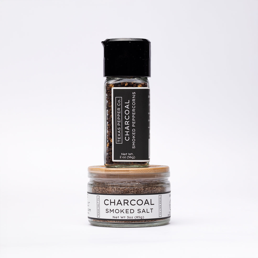 Charcoal Smoked Peppercorn in a grinder jar stacked with matching bamboo-lid Charcoal Smoked Salt jar, both with black and white labels