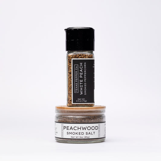 White Peach Smoked Peppercorn with grinder top stacked over Peachwood Smoked Salt jar with flat bamboo lid and clean white labels